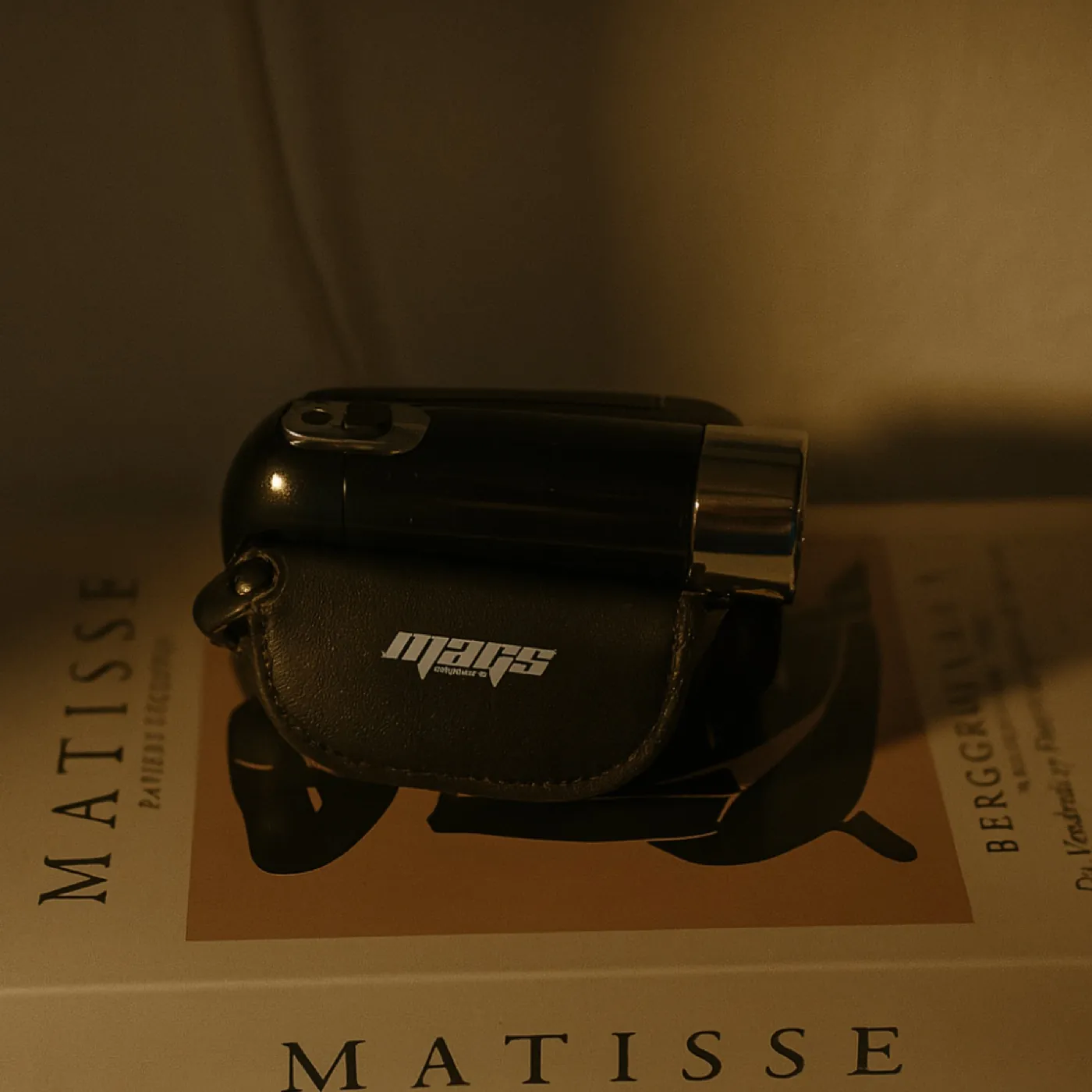 מצלמת MAGS בנרתיק עור מונחת על ספר אמנות, באור חם
